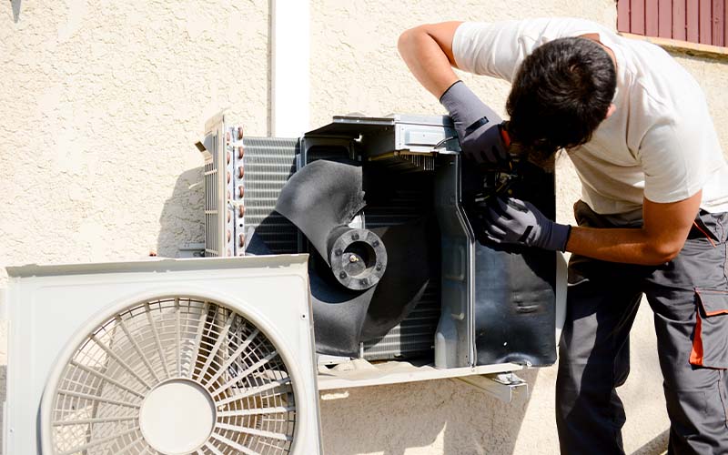 Young man AC installer working on outdoor compressor unit air conditioner at a client's home