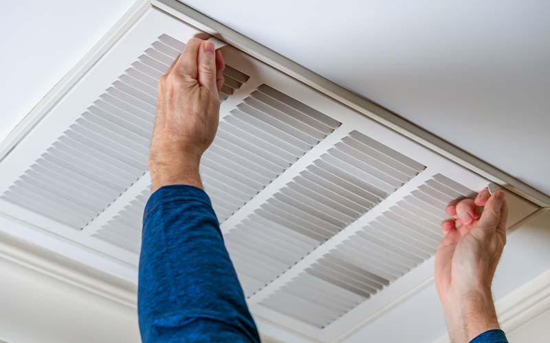 Man opening ceiling air vent to replace dirty HVAC air filter.