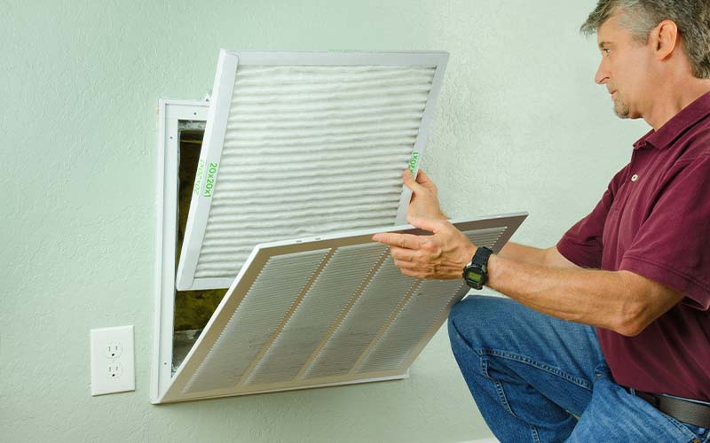 Professional AC tech installing a clean new air filter on a house air conditioner